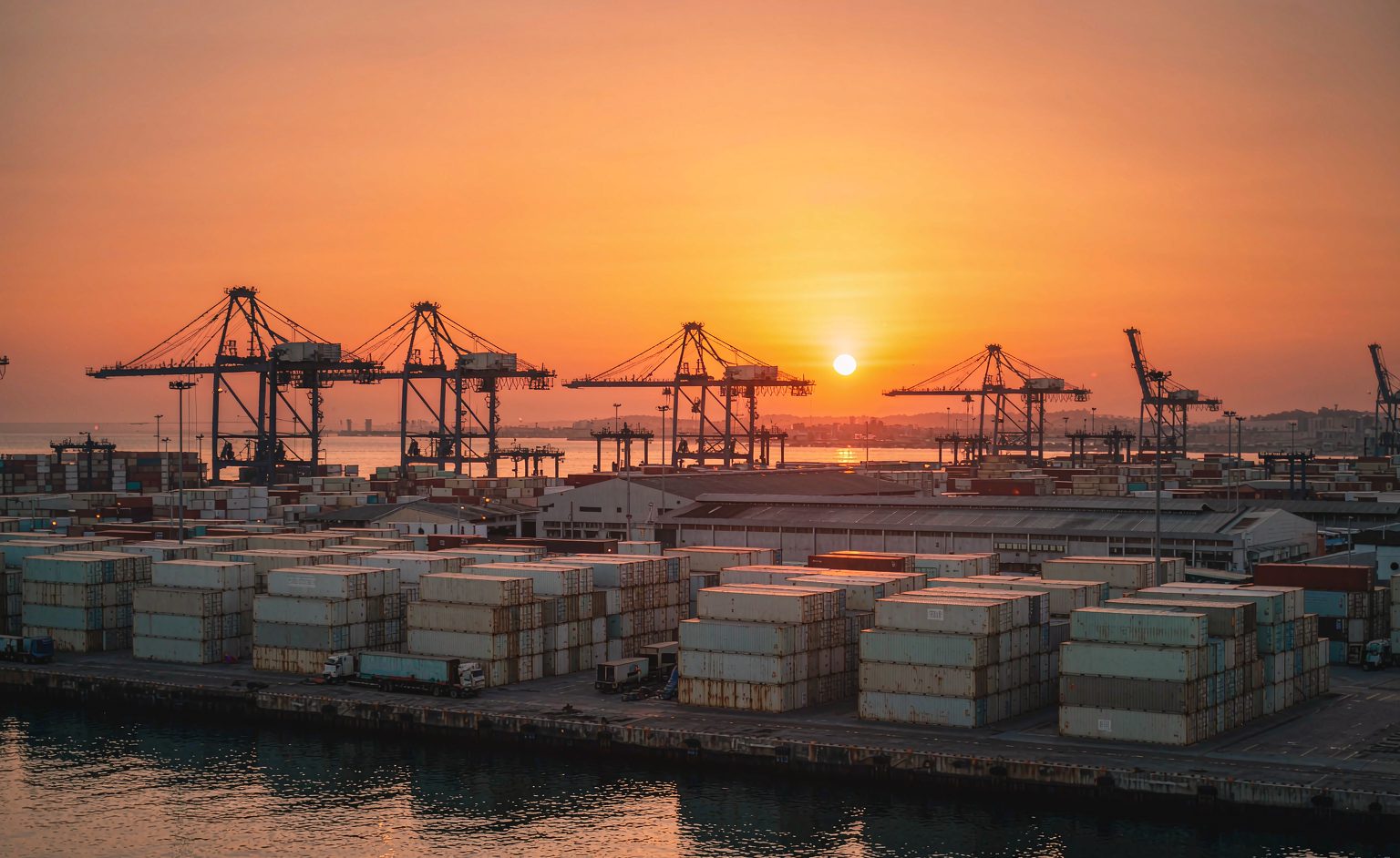 Container port terminal with stacked containers and gantry cranes at golden hour